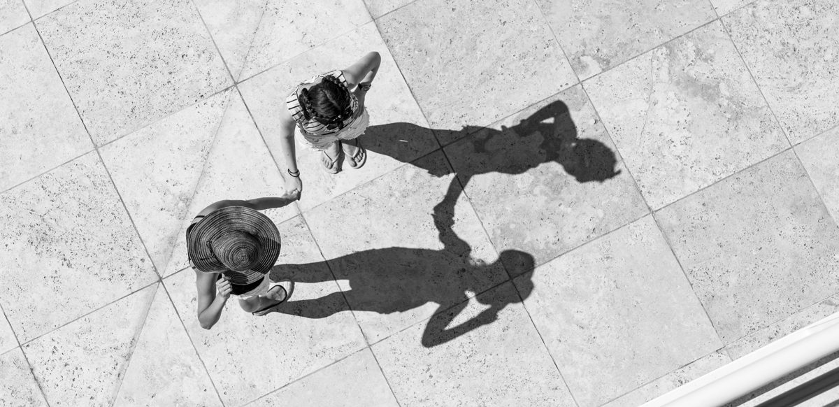 Deux personnes se tenant la main vues du dessus sur un parvis, avec leurs ombres