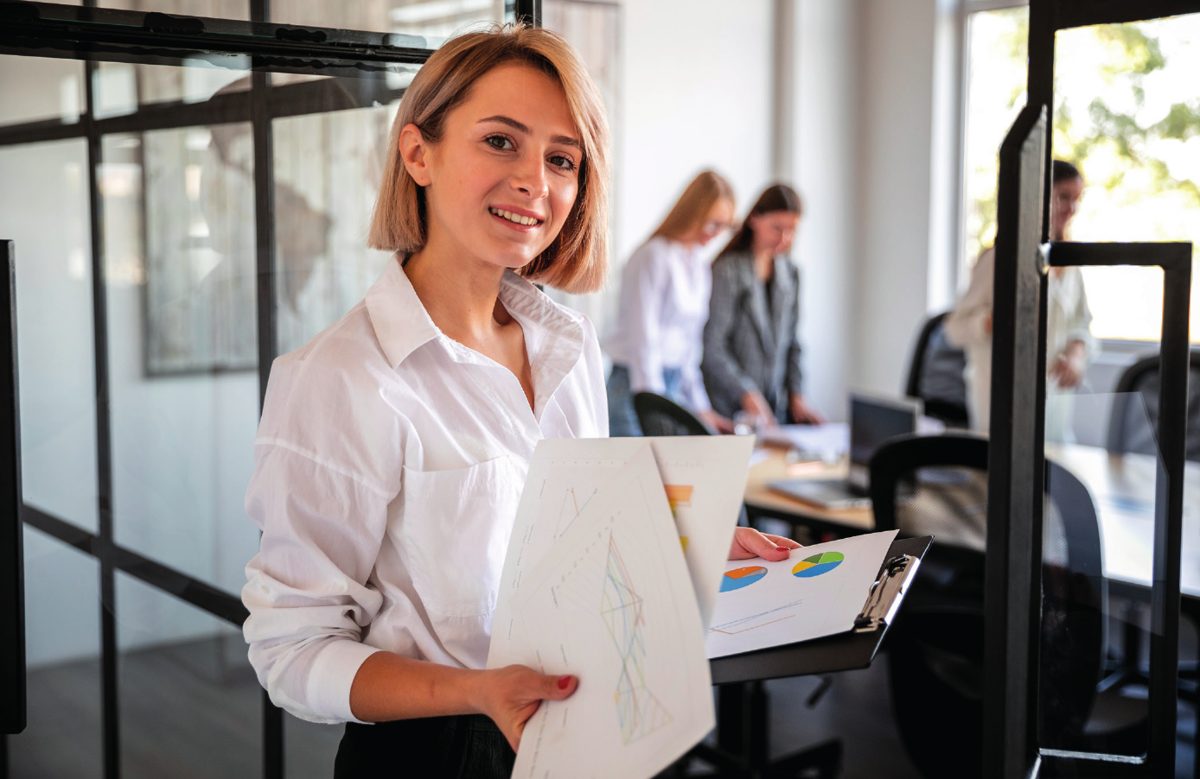 Collaboratrice souriante tenant des documents avec des graphiques dans un bureau
